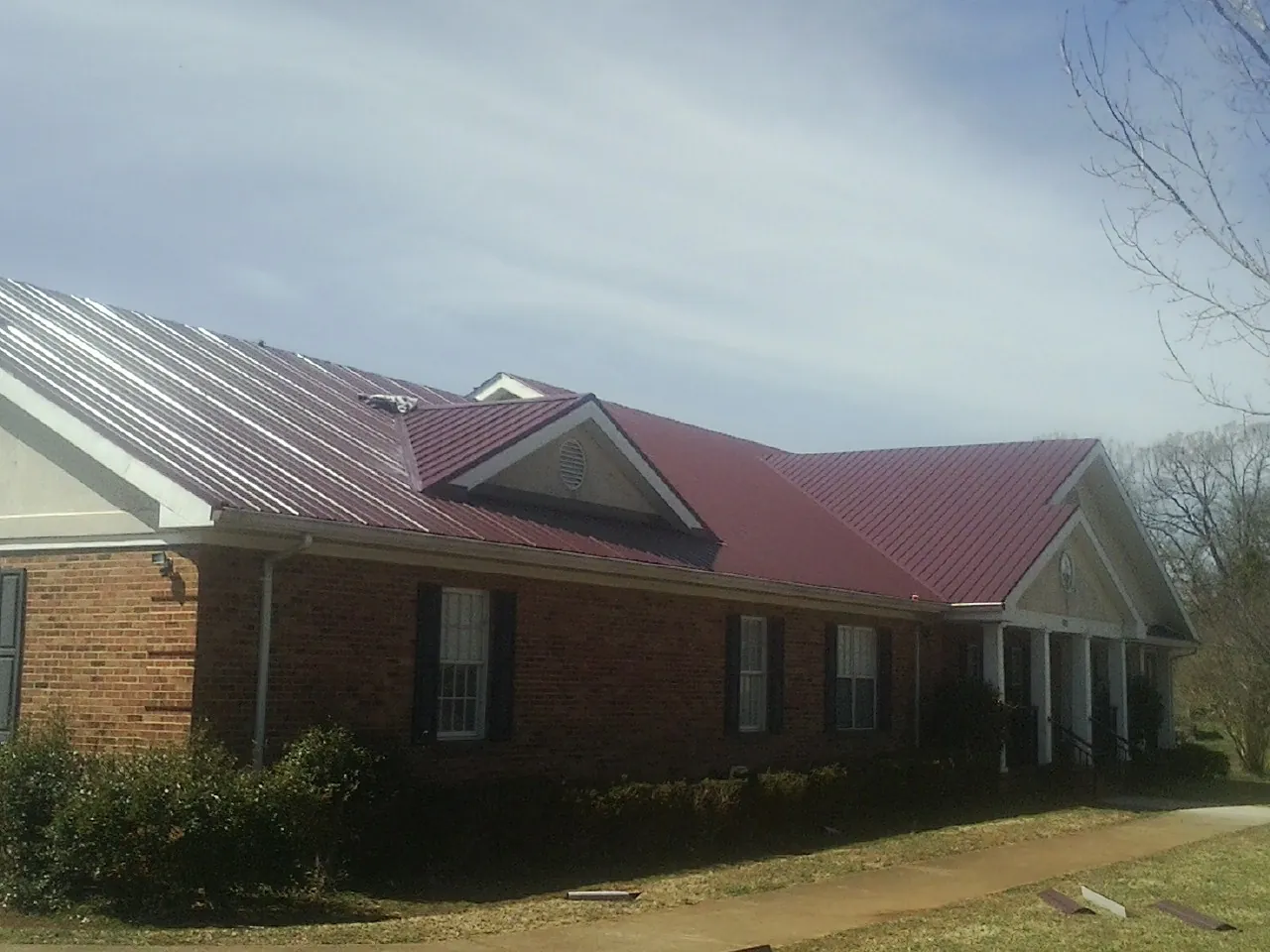 Red metal roof with gabled entries on a long brick building, from a Hail Damage Roof Repair job in Luverne