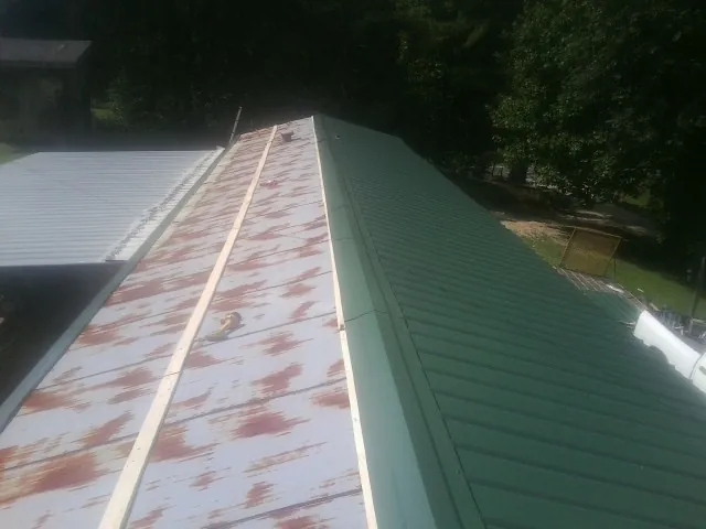 Old rusted panels beside newly installed green metal roofing — Wind Damage Roof Repair by Roofing Brothers in Luverne