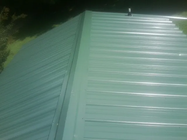 New green metal panels meeting at the ridge of a roof — Flat Roof Repair work by our crew in Luverne